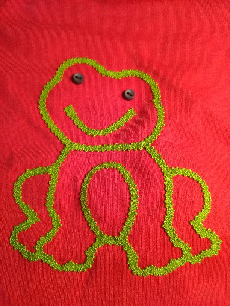 Detalle de aplicación en camiseta infantil. Encaje de cinta realizado encaje de bolillos y aplicado con punto escondido. Diseño y Ejecución de Mª José Rosel.
